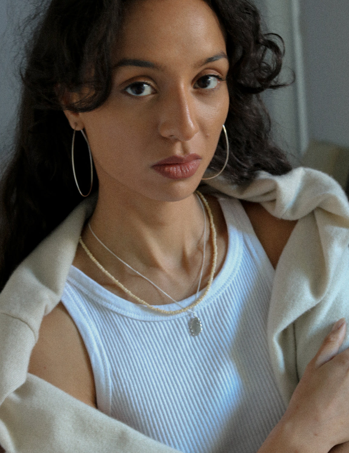 Woman wearing a white tank top and beige cardigan with sterling silver hoop earrings.