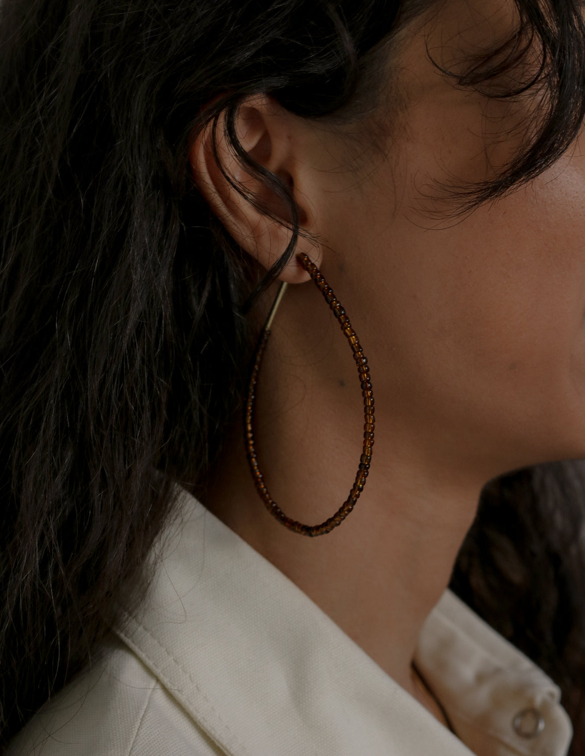 Close-up of a person wearing large hoop earrings with a neutral background
