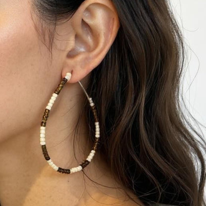 Woman wearing brown and white beaded hoop earrings with a neutral background