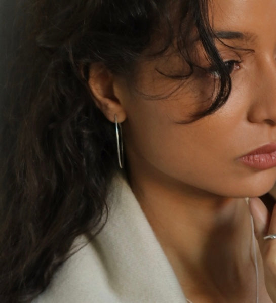 Close-up of a woman wearing a silver hoop earring with a dark background