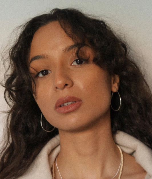Woman with curly hair wearing sterling silver hoop earrings against a neutral background